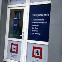 Wejście do biura Warta z naklejkami informacyjnymi na szybach: Ubezpieczenia komunikacyjne, domów, firm, na życie i majątkowe. Na dole naklejki z symbolem samochodu i domu.