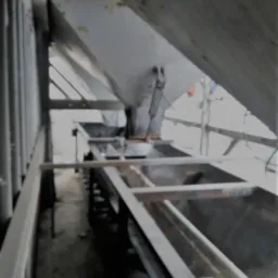 Wnętrze konstrukcji stalowej, być może w trakcie budowy lub konserwacji, z widocznymi elementami nośnymi i podtrzymującymi, ujęcie z dołu, z fragmentem białego elementu w dolnej części kadru.