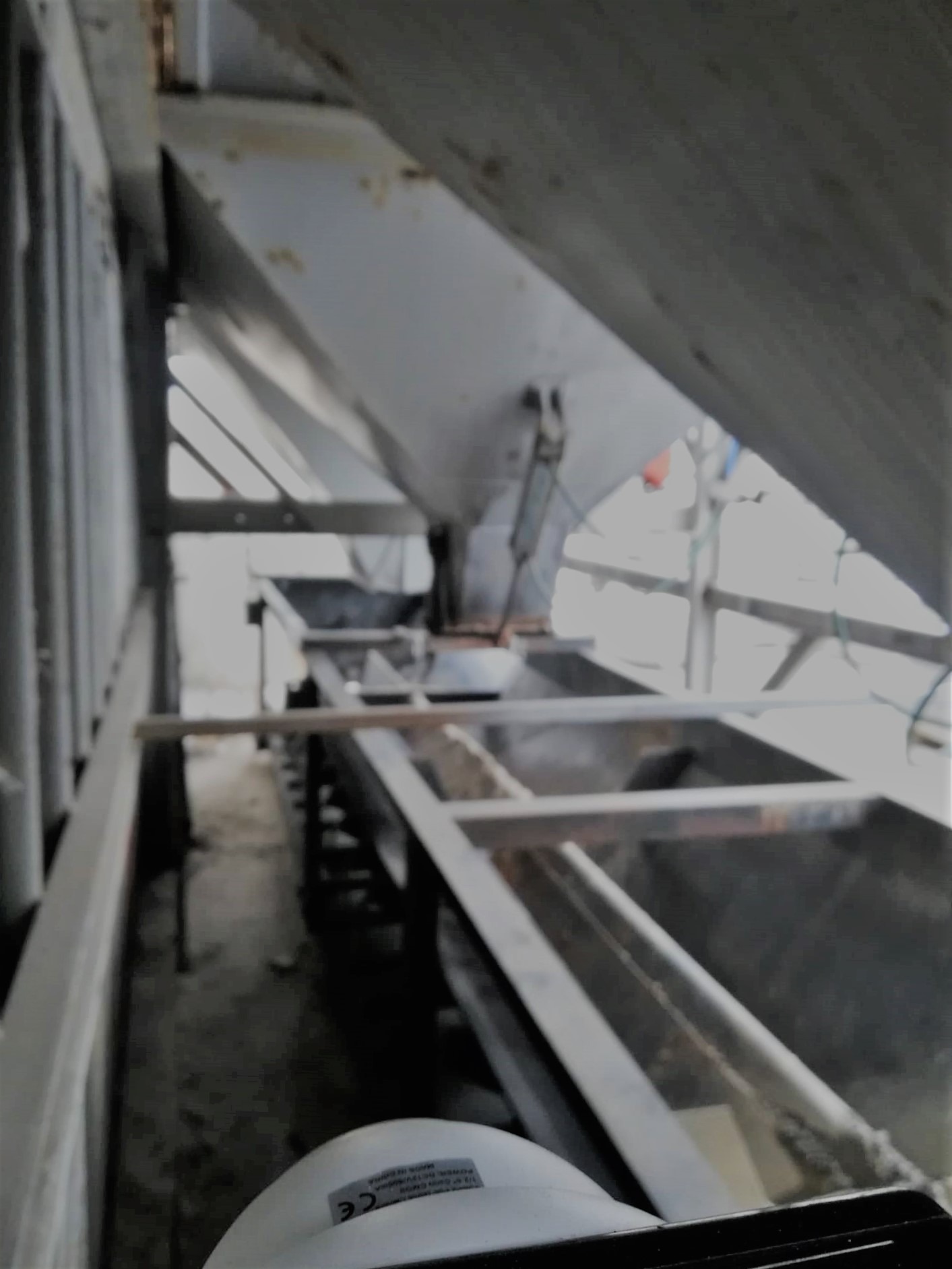 Wnętrze konstrukcji stalowej, być może w trakcie budowy lub konserwacji, z widocznymi elementami nośnymi i podtrzymującymi, ujęcie z dołu, z fragmentem białego elementu w dolnej części kadru.