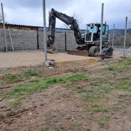 Teren budowy z mini koparką Terex, przygotowany pod fundamenty z widocznymi słupami i podsypką żwirową, błotniste podłoże w tle.