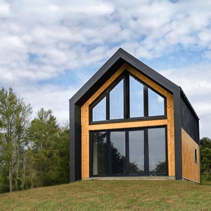 Nowoczesny, parterowy budynek z drewna i czarnej blachy, z dużymi oknami wychodzącymi na zalesione wzgórze.