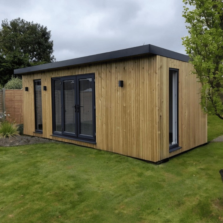 Nowoczesny budynek z drewnianą elewacją w pionowe deski, płaski dach, szare okna i drzwi, oświetlenie zewnętrzne, otoczony trawnikiem i zielenią.