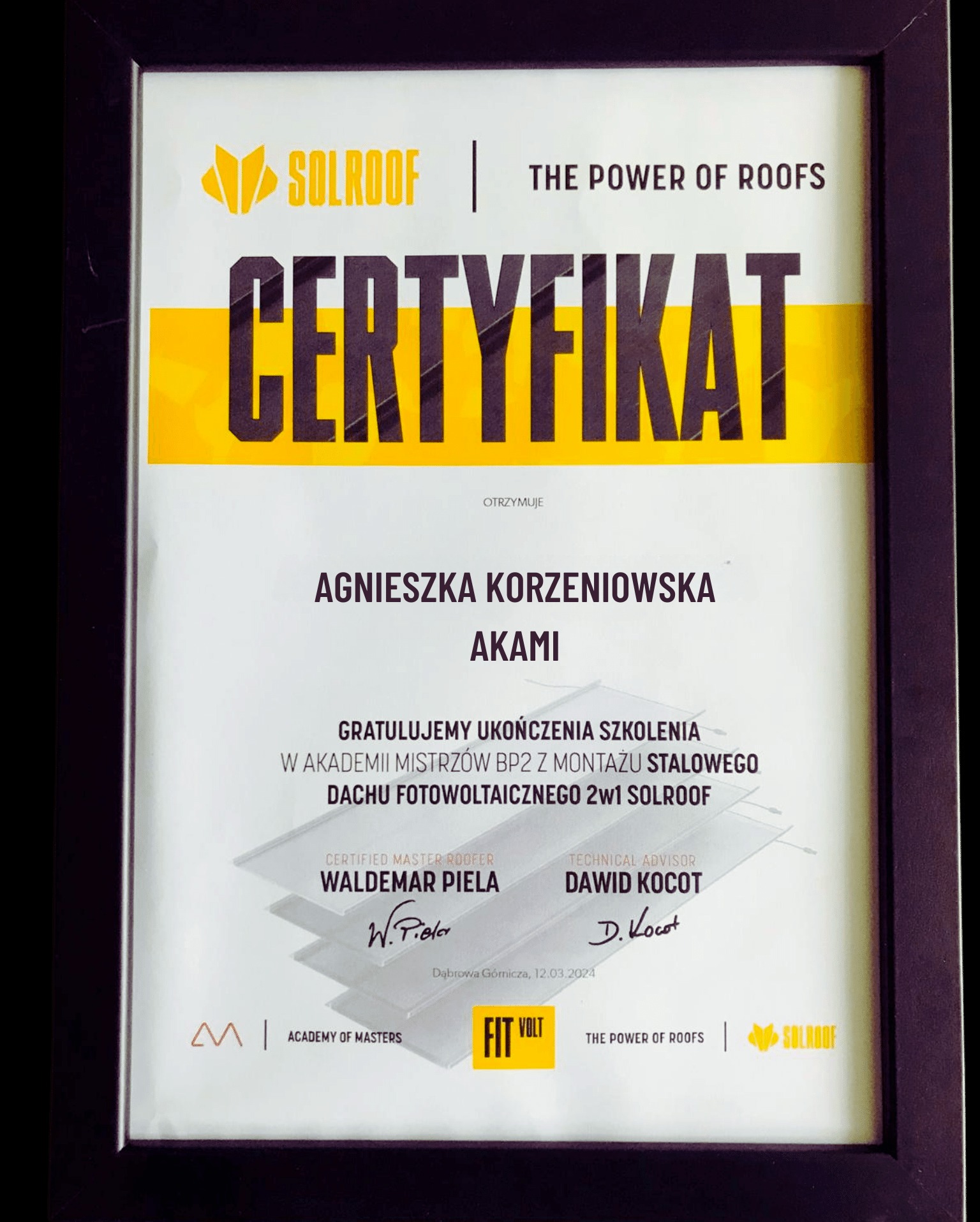 Oprawiony w ramkę certyfikat firmy Solroof potwierdzający ukończenie szkolenia z montażu stalowego dachu fotowoltaicznego przez Agnieszkę Korzeniowską z Akademii Mistrzów, z podpisami Waldemara...