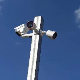 Trzy kamery na metalowym słupie, skierowane w różnych kierunkach, na tle błękitnego nieba z chmurami.