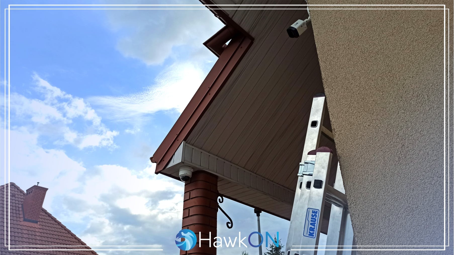 Dwie kamery kopułkowe zamontowane pod okapem budynku, aluminiowa drabina Kraus obok ściany o szorstkiej fakturze, błękitne niebo w tle.