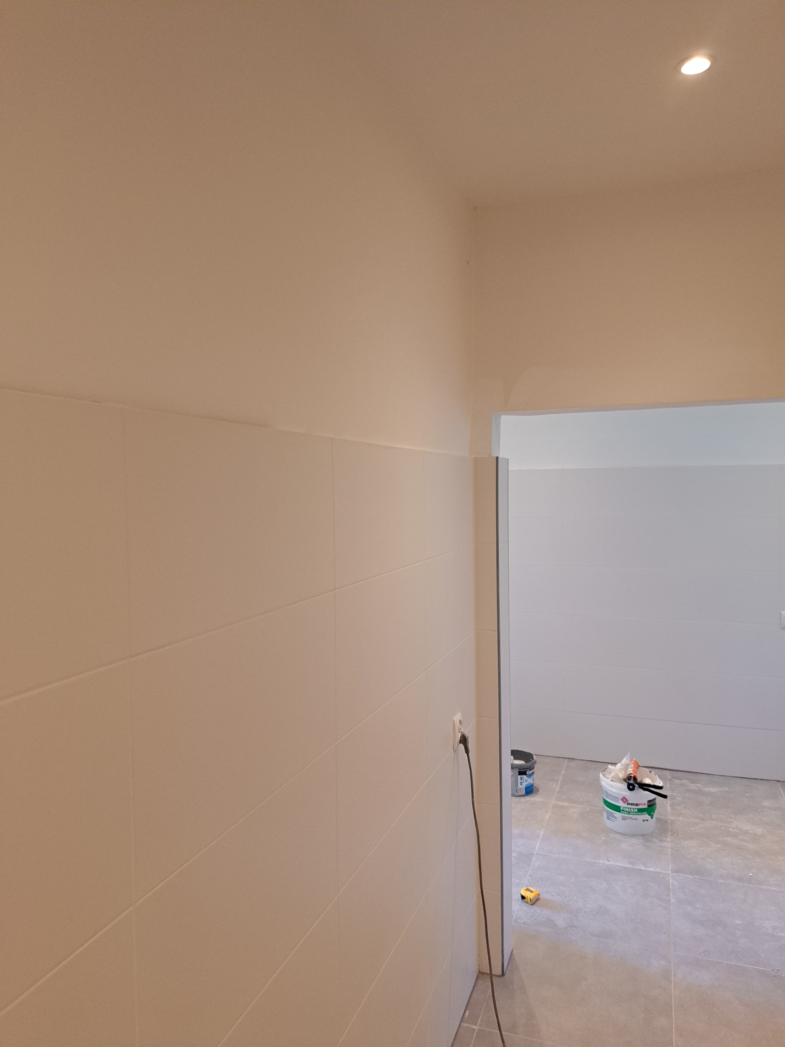 Wykończona łazienka z białymi płytkami, widoczna puszka z zaprawą i narzędzia. Świeże fugi i minimalistyczne oświetlenie punktowe.