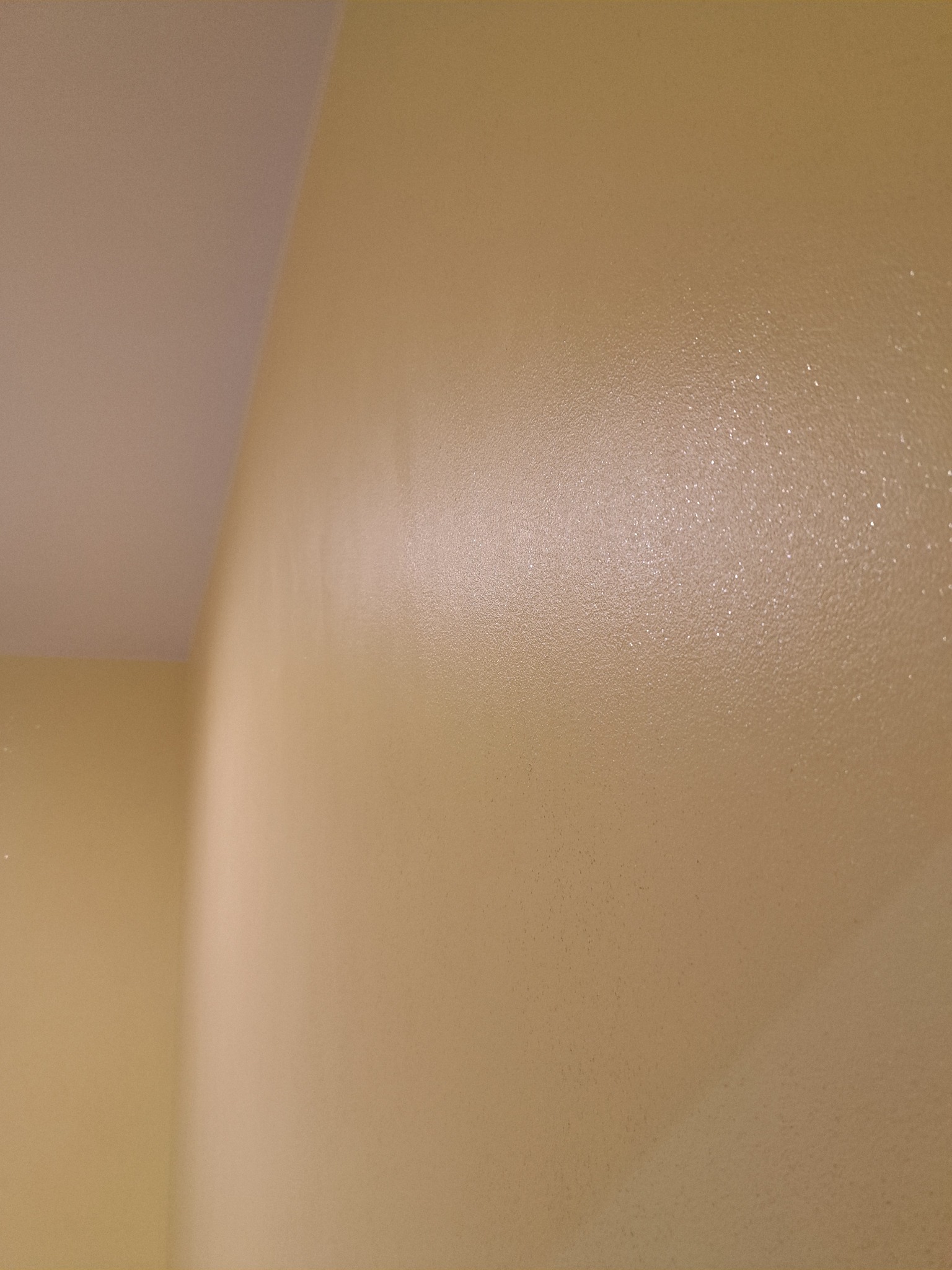 Ściana w odcieniach beżu, świeżo po malowaniu, z widoczną fakturą i delikatnym połyskiem. Ujęcie z bliska, ukazujące gładką powierzchnię i precyzję wykonania.