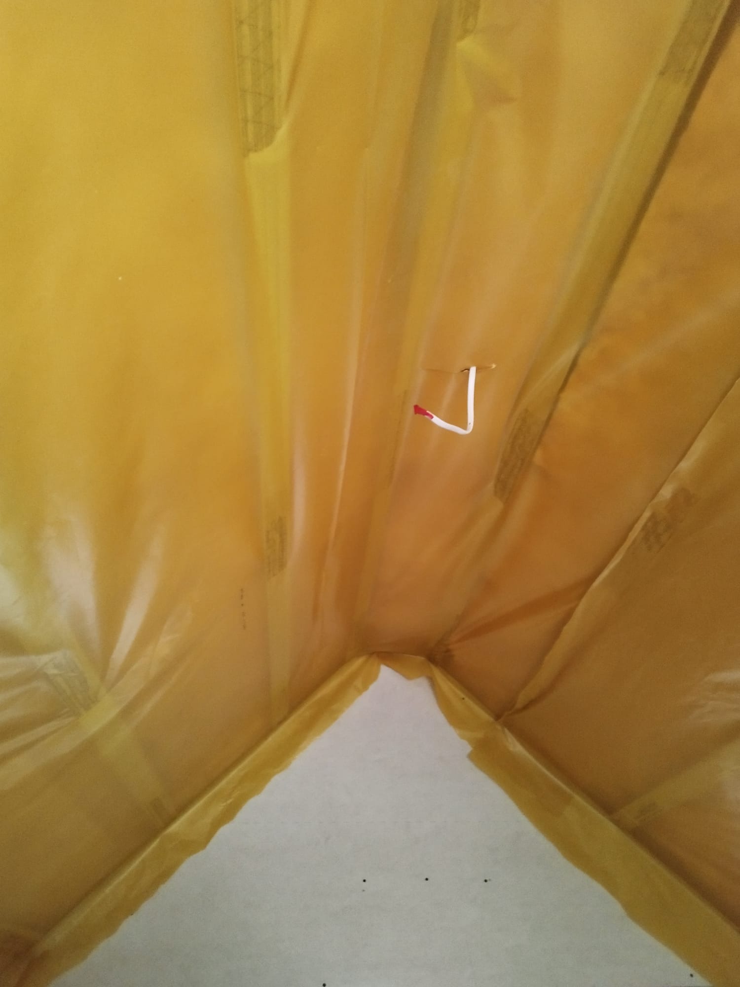 Żółta folia paroizolacyjna na poddaszu, zabezpieczająca przed wilgocią, z widocznym fragmentem ściany z płyty karton-gips i wystającym kablem.