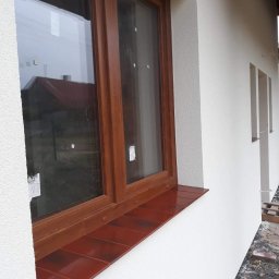 MARTOS Usługi budowlane Mariusz Gaca - Nowe, brązowe okno PCV z parapetem wykończonym klinkierem, osadzone w świeżo otynkowanej, białej elewacji budynku.