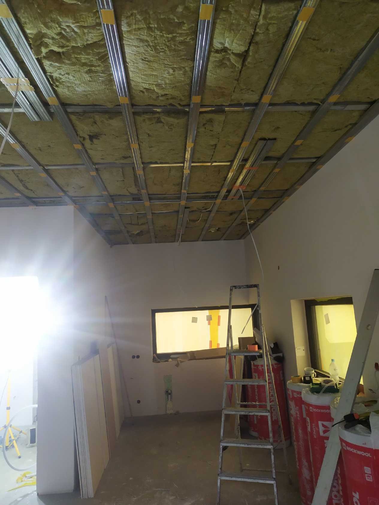 Montaż izolacji z wełny mineralnej i konstrukcji metalowej pod płytę karton gips na suficie w trakcie remontu, widoczna drabina i materiały budowlane.