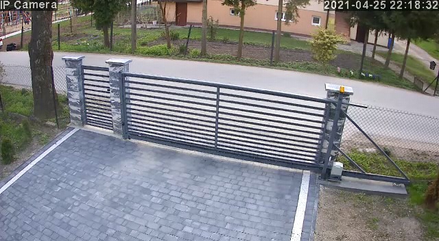 Automatyczna brama przesuwna z poziomymi profilami, zamontowana na posesji z kostką brukową, widok z kamery IP, data i godzina na zdjęciu.