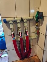 Rozdzielacz instalacji grzewczej z czterema obwodami, rury w izolacji termicznej, zamontowany na kafelkowanej ścianie w pomieszczeniu technicznym.