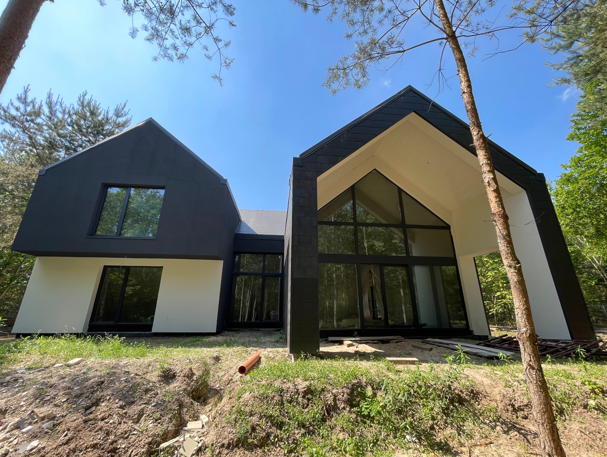 Nowoczesny dom z dużymi oknami, czarno-biała elewacja, zielone otoczenie. Widok z dołu, podkreślający architekturę i przeszklenia. Częściowo widoczna rura na trawie.