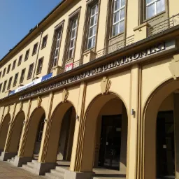 Odnowiona fasada budynku uczelni w kolorze piaskowym, z rzędem łukowych wejść i napisem 'Wydział Inżynierii Mechanicznej i Mechatroniki' nad wejściami.