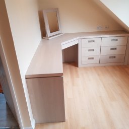 Sebko - Jasna, drewniana toaletka z lustrem i szufladami, wbudowana w skos poddasza, z widocznymi gniazdkami elektrycznymi na ścianie i parkietem na podłodze.