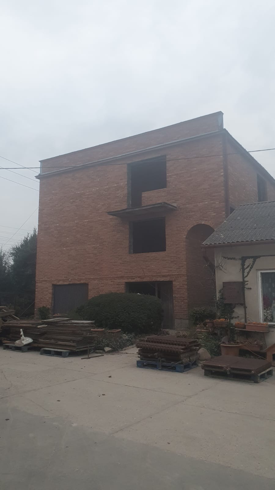 Ceglany budynek w trakcie renowacji w Warszawie, widoczne otwarte okna i zgromadzone materiały budowlane na zewnątrz.