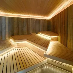 Wnętrze nowoczesnej, drewnianej kabiny, z wielopoziomowymi ławkami podświetlonymi listwami LED, wykończonej panelami z surowego drewna.