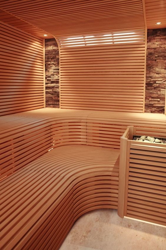 Wnętrze nowoczesnej kabiny, wyłożonej jasnym drewnem z poziomymi listwami, z kamienną ścianą w tle i podświetlanymi ławkami o zaokrąglonych kształtach.