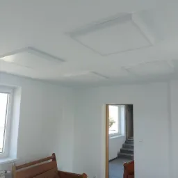 Wnętrze nowo wykończonego pokoju z czterema kwadratowymi panelami LED zamontowanymi na suficie, widok z dołu, okno z białymi ramami po lewej stronie, drzwi z widocznymi schodami w tle