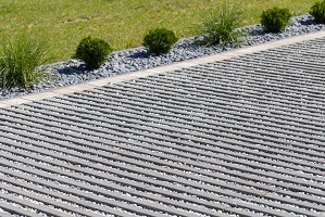 Szara, ażurowa nawierzchnia drogi z wypełnieniem z drobnych kamieni, obrzeże z kostki, trawnik w tle.