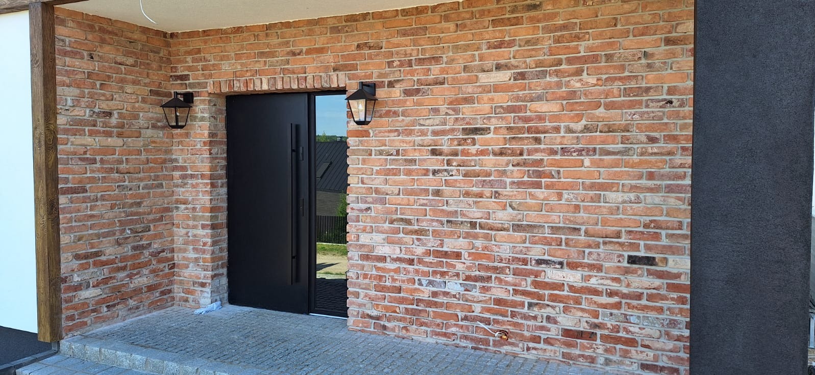 Elewacja budynku z cegły klinkierowej z czarnymi, nowoczesnymi drzwiami wejściowymi i lampami w stylu retro.