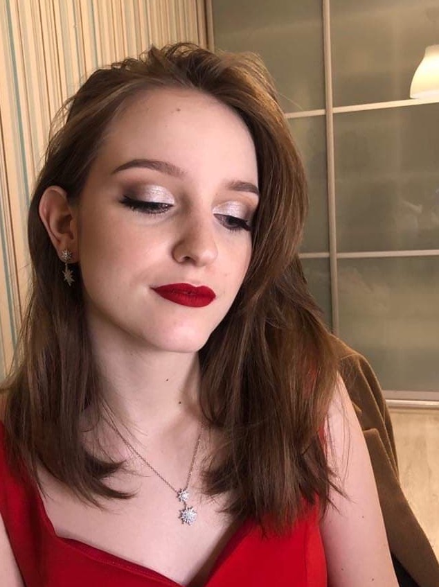 Portret kobiety z połyskującym makijażem oczu w odcieniach srebra i mocno czerwoną szminką, w czerwonej sukience z delikatną srebrną biżuterią w kształcie gwiazd.