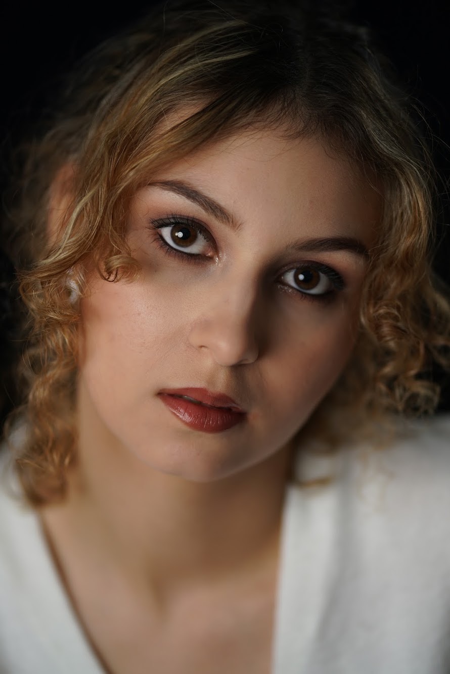 Portret kobiety z profesjonalnym makijażem, podkreślone oczy i usta w odcieniu burgundu, delikatne blond loki.