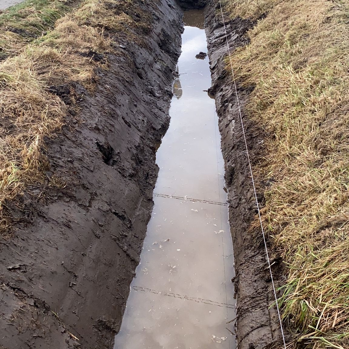 Wykop wypełniony wodą w Mechnicach, widoczna linia wyznaczająca przebieg rowu, ziemia po bokach.