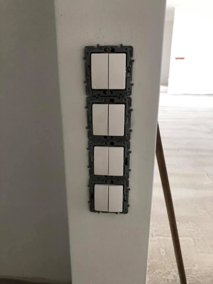 Cztery białe, podwójne włączniki światła zamontowane pionowo na pomalowanej ścianie, widoczne ślady niedokończonych prac wykończeniowych.