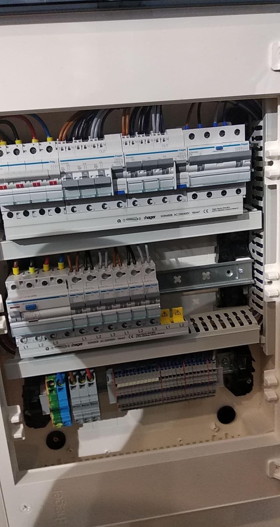 Otwarta skrzynka elektryczna z zamontowanymi bezpiecznikami i przewodami, widok z bliska na wewnętrzne elementy instalacji elektrycznej.