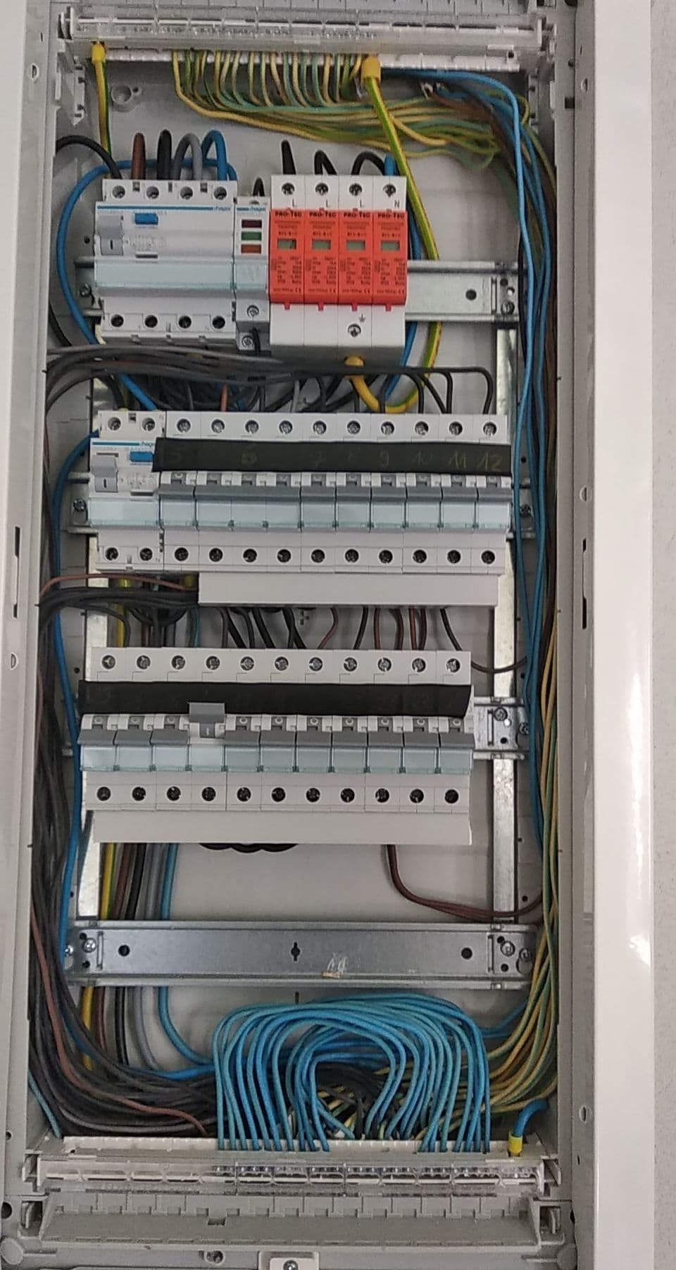 Otwarta skrzynka rozdzielcza z widocznymi bezpiecznikami, przekaźnikami i uporządkowanymi przewodami w kolorach niebieskim, żółto-zielonym i brązowym.
