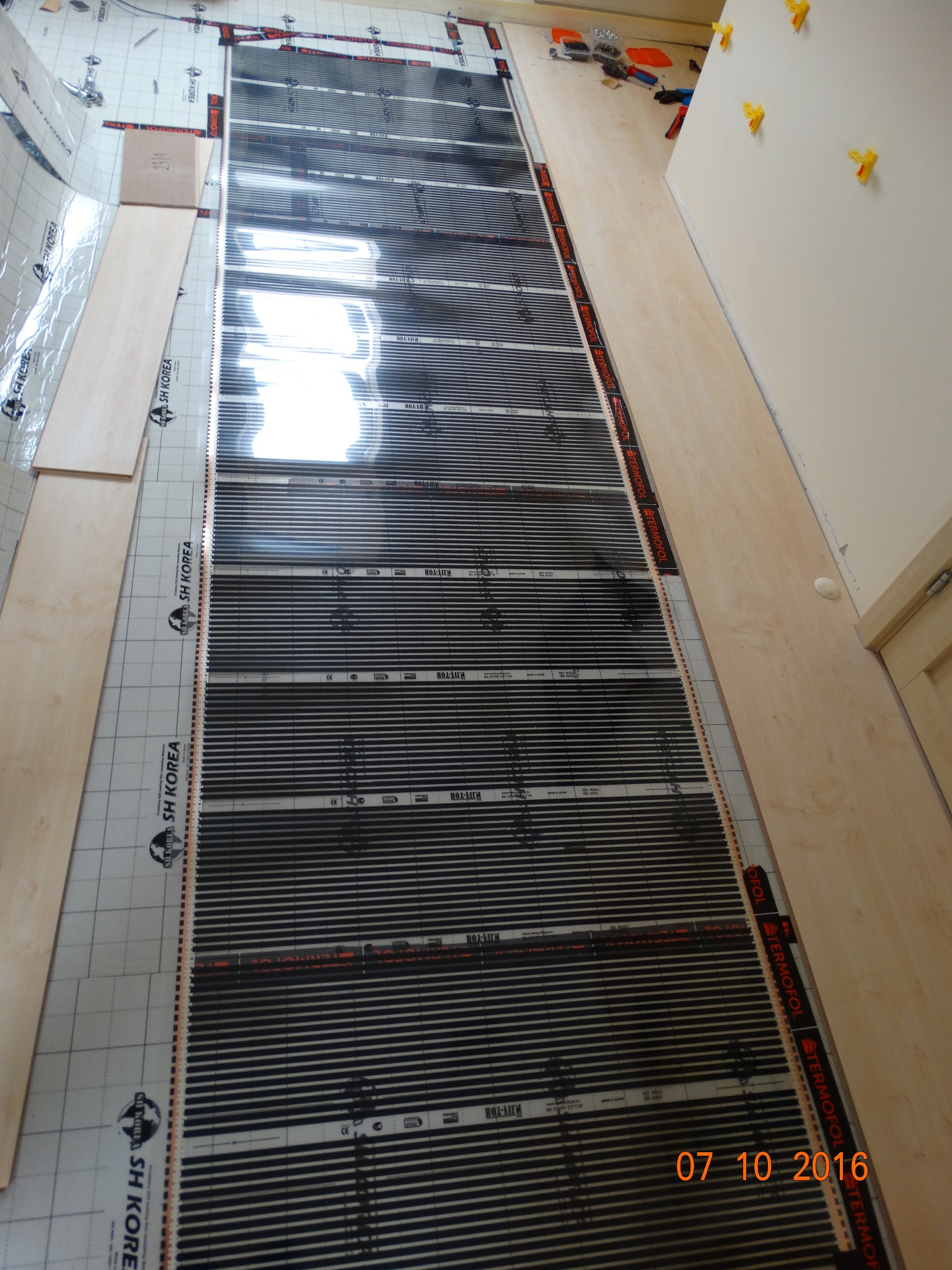 Rozkładanie maty grzewczej na podłodze z widocznymi panelami podłogowymi i narzędziami w tle, widok z góry, data wykonania 07 10 2016.