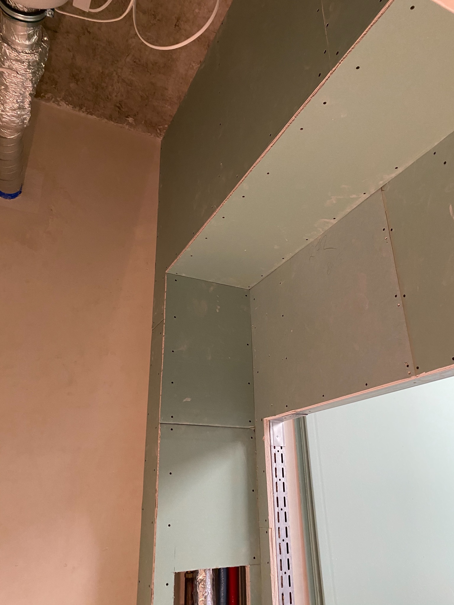 Konstrukcja z płyt kartonowo-gipsowych w trakcie montażu, widoczne profile metalowe, instalacja wentylacyjna i fragment ściany z widoczną strukturą betonu.