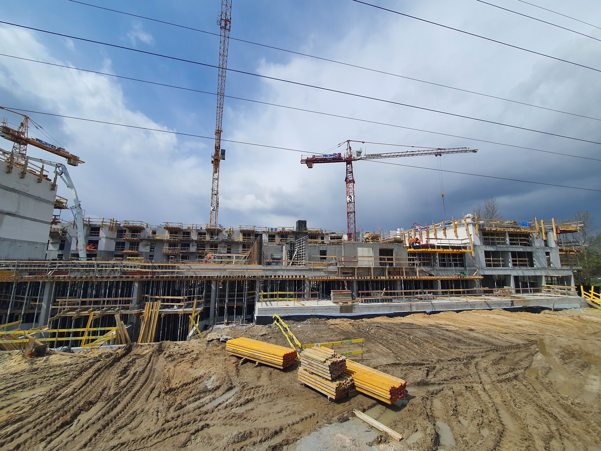 Wznoszenie wielopiętrowego budynku żelbetowego w Krakowie, widoczne szalunki, dźwigi i składowane elementy konstrukcyjne na placu budowy.