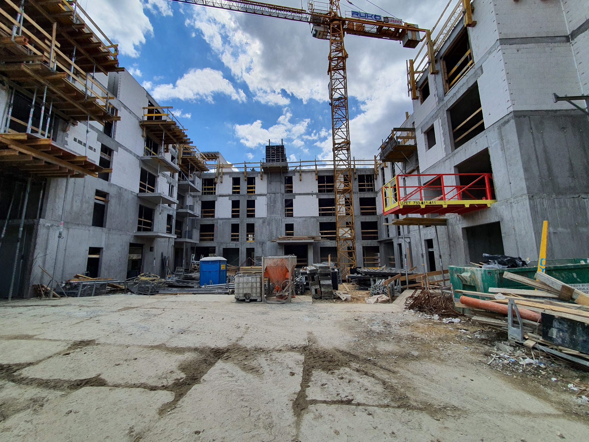 Budowa wielopiętrowego budynku z betonu komórkowego i żelbetu, widoczne rusztowania, dźwig budowlany i materiały budowlane na placu budowy.