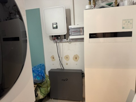 Zestaw urządzeń: inwerter, rozdzielnica i akumulator Fox, tworzące instalację do magazynowania energii. Białe ściany, widoczne przewody.