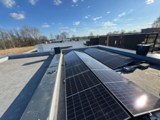 Panele słoneczne na płaskim dachu domu jednorodzinnego w słoneczny dzień. Widok z góry, lekki kąt. Czyste niebo, nowoczesna architektura w tle.