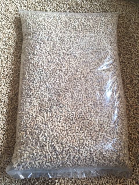 Worek przezroczysty wypełniony jasnymi pelletami drzewnymi, widoczne struktury drewna, tło z rozsypanego pelletu.