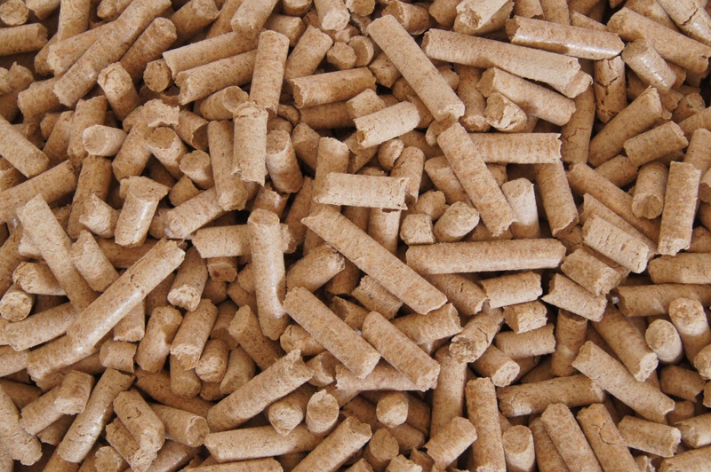 Stos pelletu drzewnego w jasnym oświetleniu, widoczne drobne wióry i tekstura drewna.