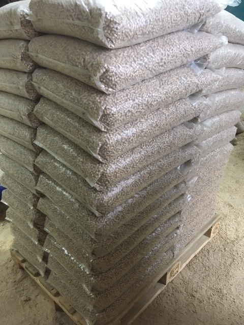 Stos worków z pelletem ułożonych na drewnianej palecie, widoczne drobne trociny na podłożu.