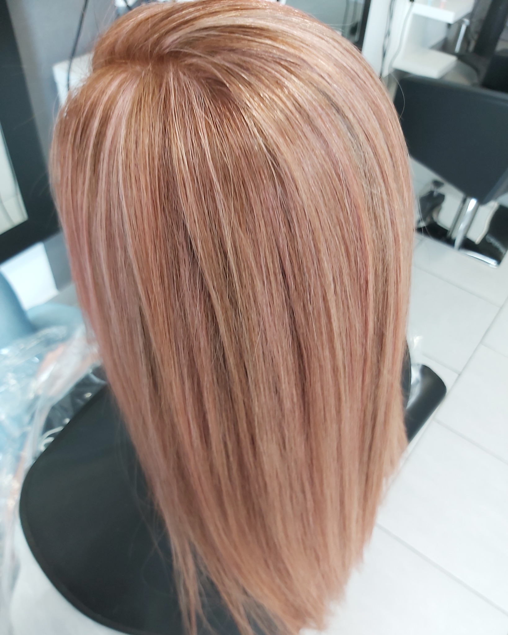 Proste, długie włosy w odcieniu cukierkowego blondu, widok z tyłu na czarnym fotelu fryzjerskim.