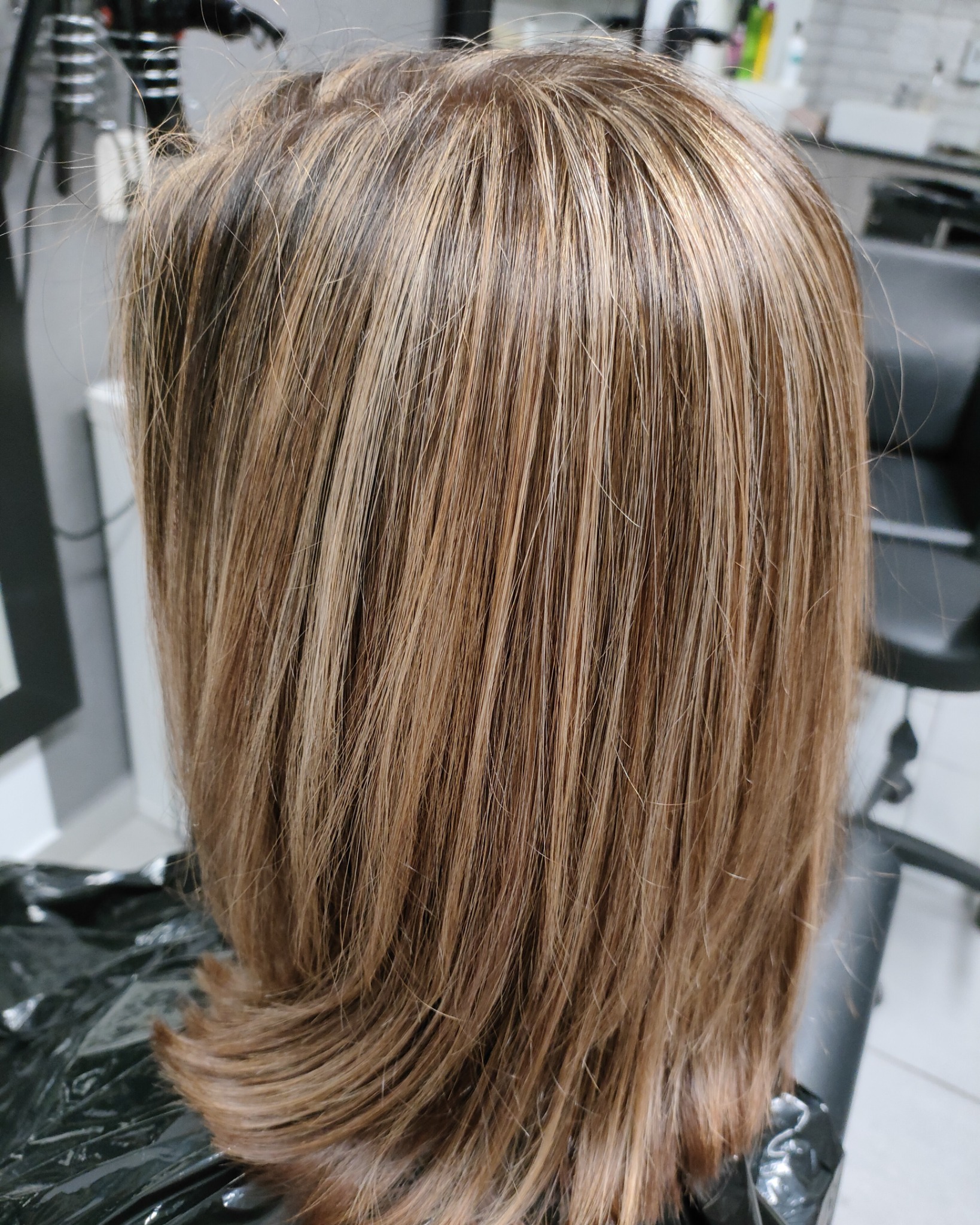Tył głowy z brązowymi włosami z blond pasemkami, świeżo po koloryzacji w salonie fryzjerskim.