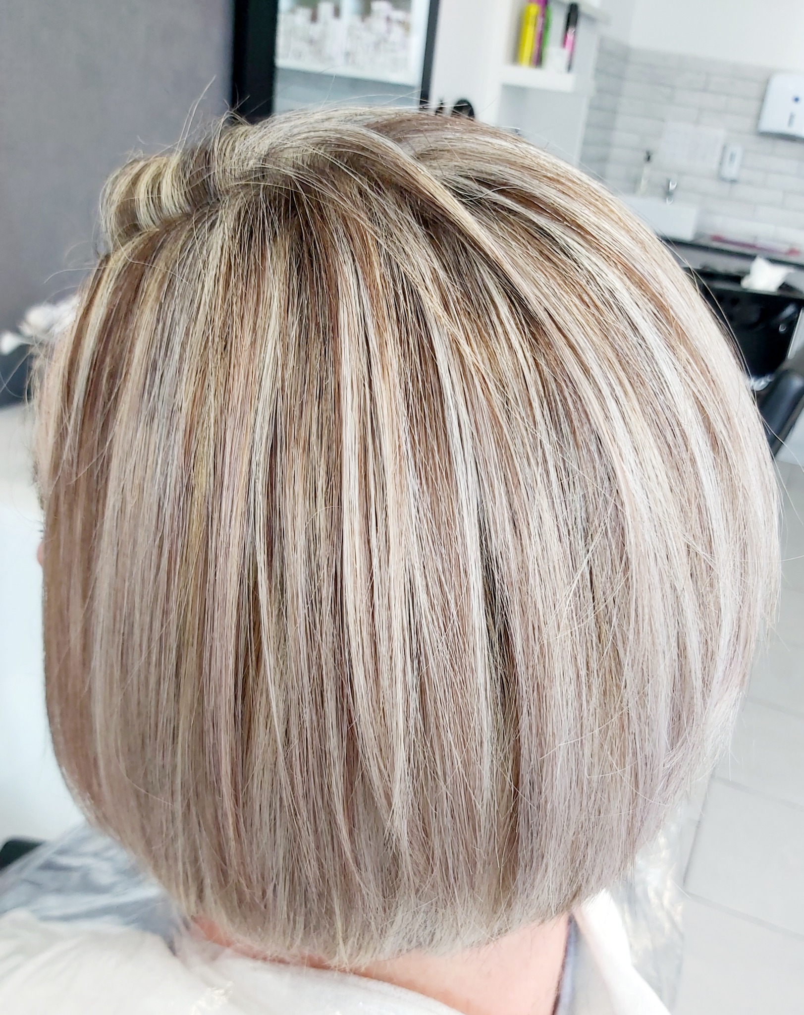 Blond włosy po koloryzacji z widocznymi odrostami w chłodnym odcieniu, krótka fryzura typu bob, widok z tyłu.