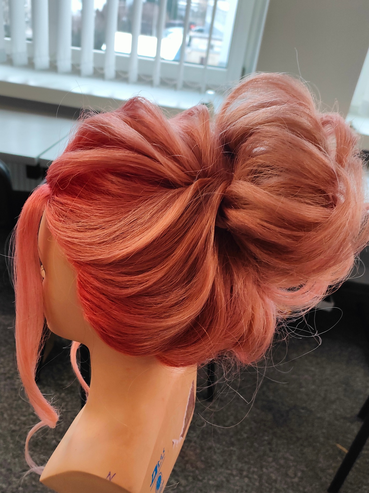 Upięcie z różowych włosów na manekinie, z widoczną asymetryczną fryzurą i pojedynczym pasmem opadającym z boku.