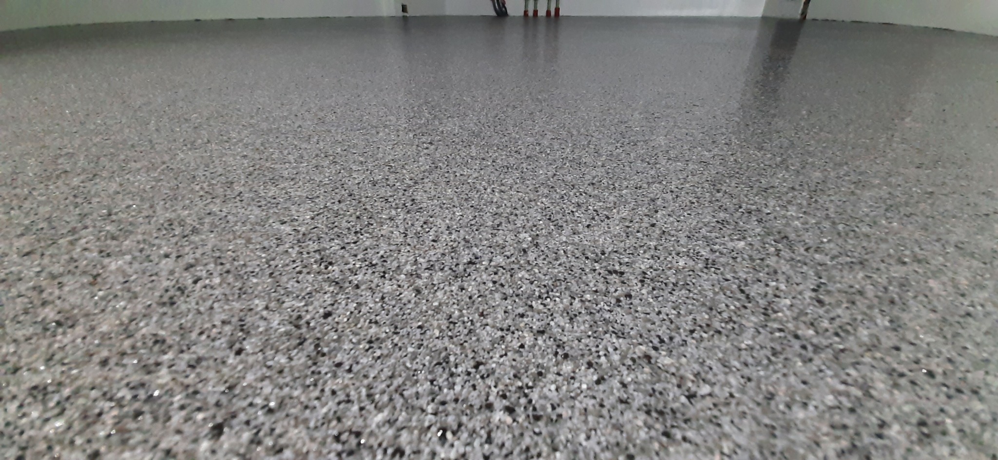 Szara, jednolita posadzka z drobnymi, ciemnymi kamyczkami, delikatnie połyskująca, sfotografowana pod kątem z niskiej perspektywy.