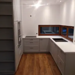 Frezowane fronty lakierowane, blat wpuszczany pod okno zastępuje tradycyjny parapet i poszerza pole robocze.