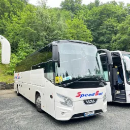 Biały autokar marki VDL SpeedBus zaparkowany na żwirowym parkingu, z zielonymi drzewami w tle, widoczna tablica rejestracyjna WGM 3754J.