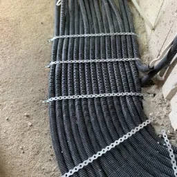 Równe rzędy czarnych, karbowanych rur instalacyjnych przymocowanych do podłoża za pomocą perforowanych, metalowych taśm mocujących i wkrętów.