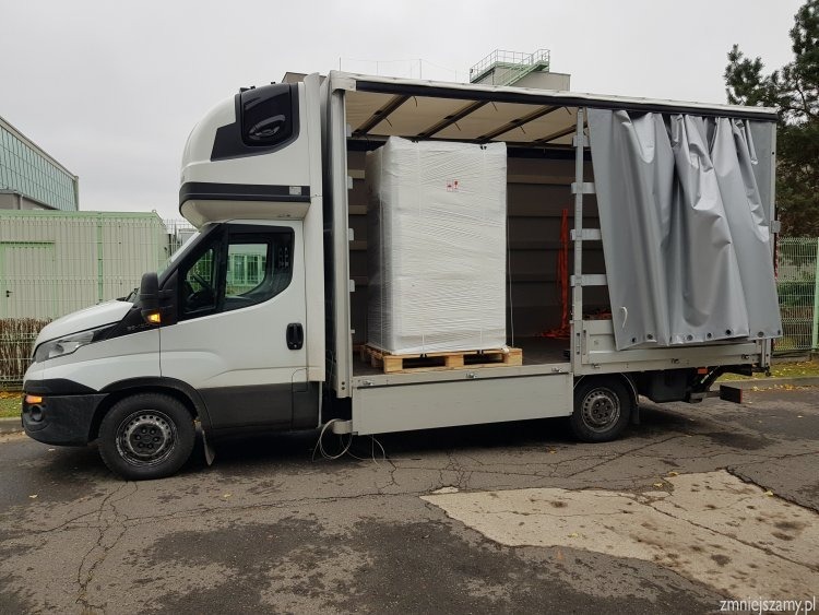 Biały bus z otwartą przestrzenią ładunkową, w której znajduje się zapakowany na palecie ładunek, zabezpieczony folią.