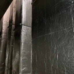 Izolacja termiczna przewodów wentylacyjnych owinięta srebrną folią aluminiową, mocowana metalowymi uchwytami.